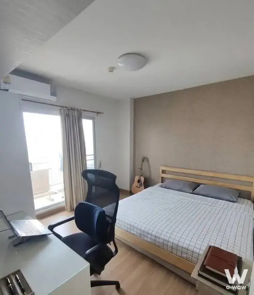 Bright bedroom in a Supalai Park condo with light-wood slat bed, ergonomic chair, and acoustic guitar