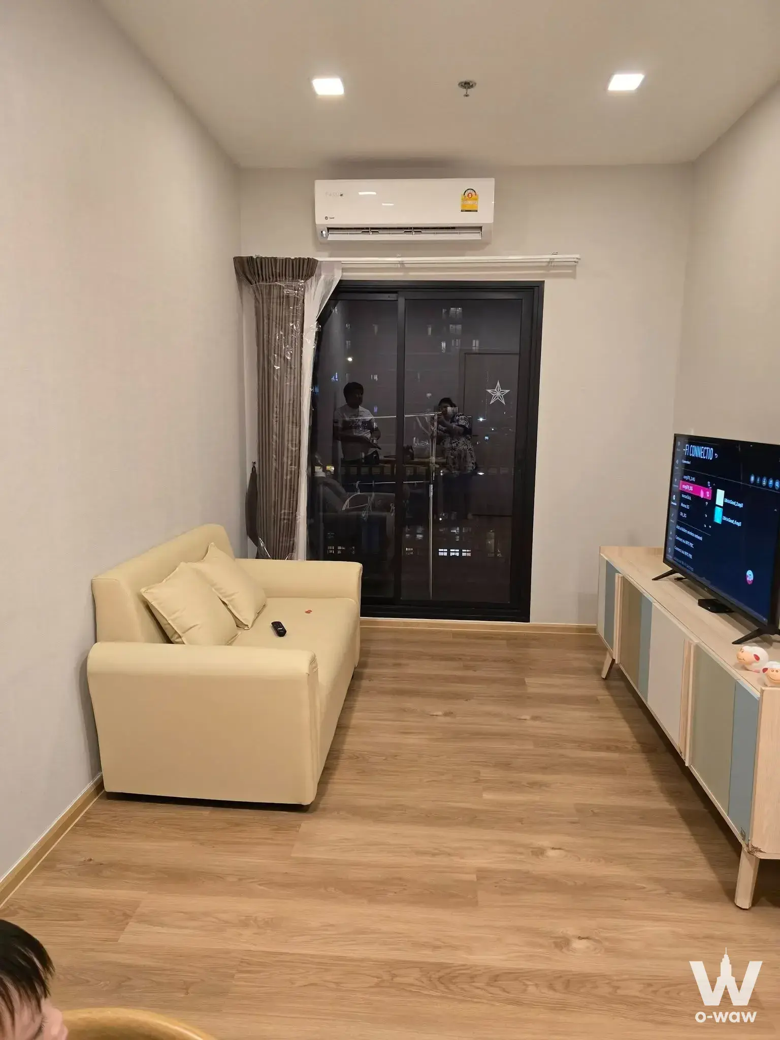 Living room in Metris Rama 9 condo with cream leather sofa and glass sliding doors opening to a city view