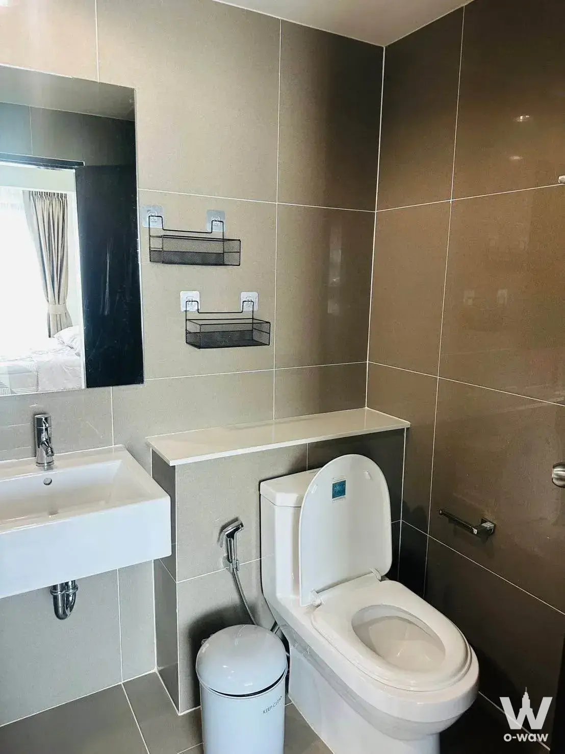 The bathroom in a 1-bed Centrio Condominium Phuket condo has beige tiles, a wall sink and a mirror