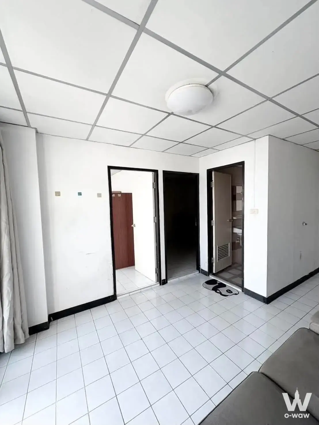 Empty living room in a Phasuk Place condo showing white tile floors and three black-framed doorways