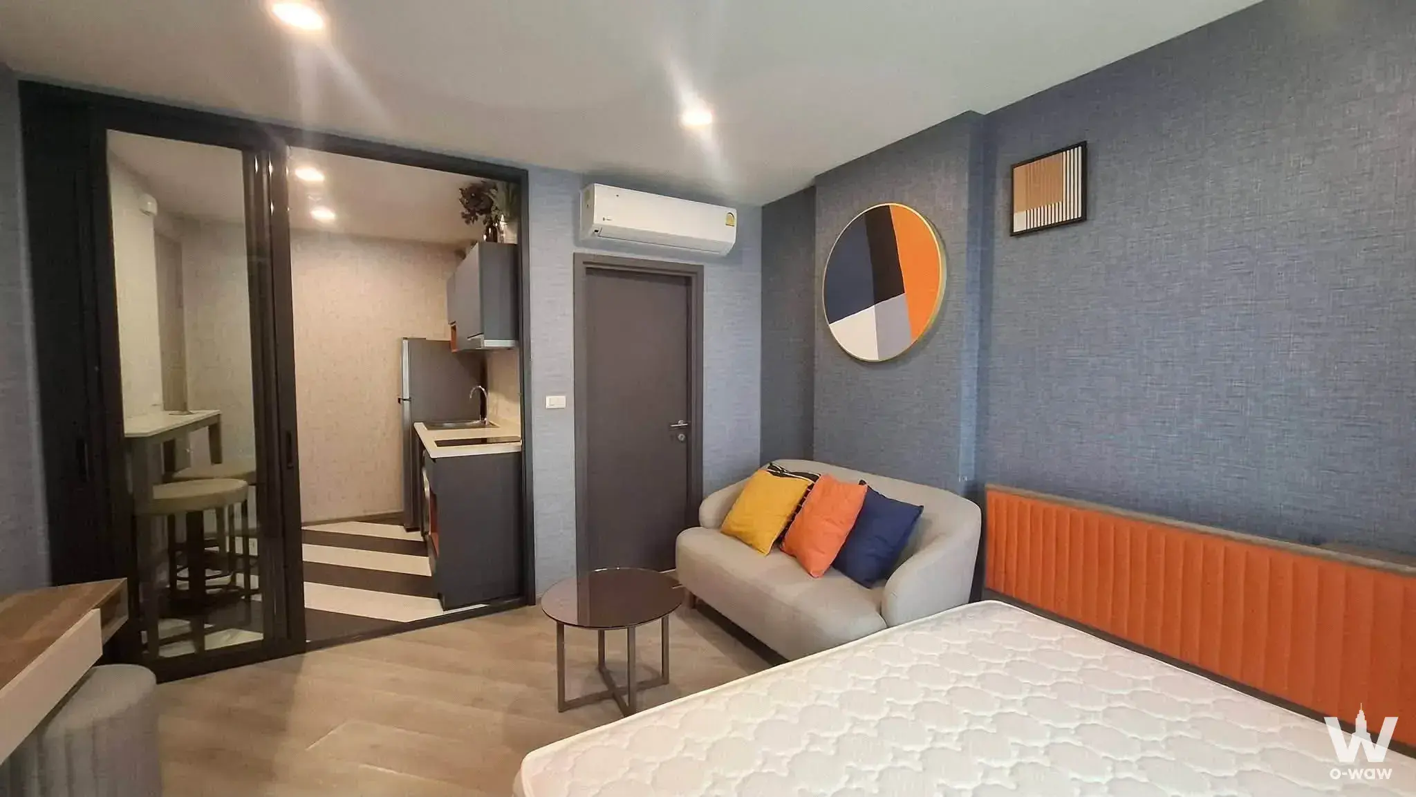 Furnished studio at THE BASE Saphanmai featuring an orange slat headboard and glass partitioned kitchenette