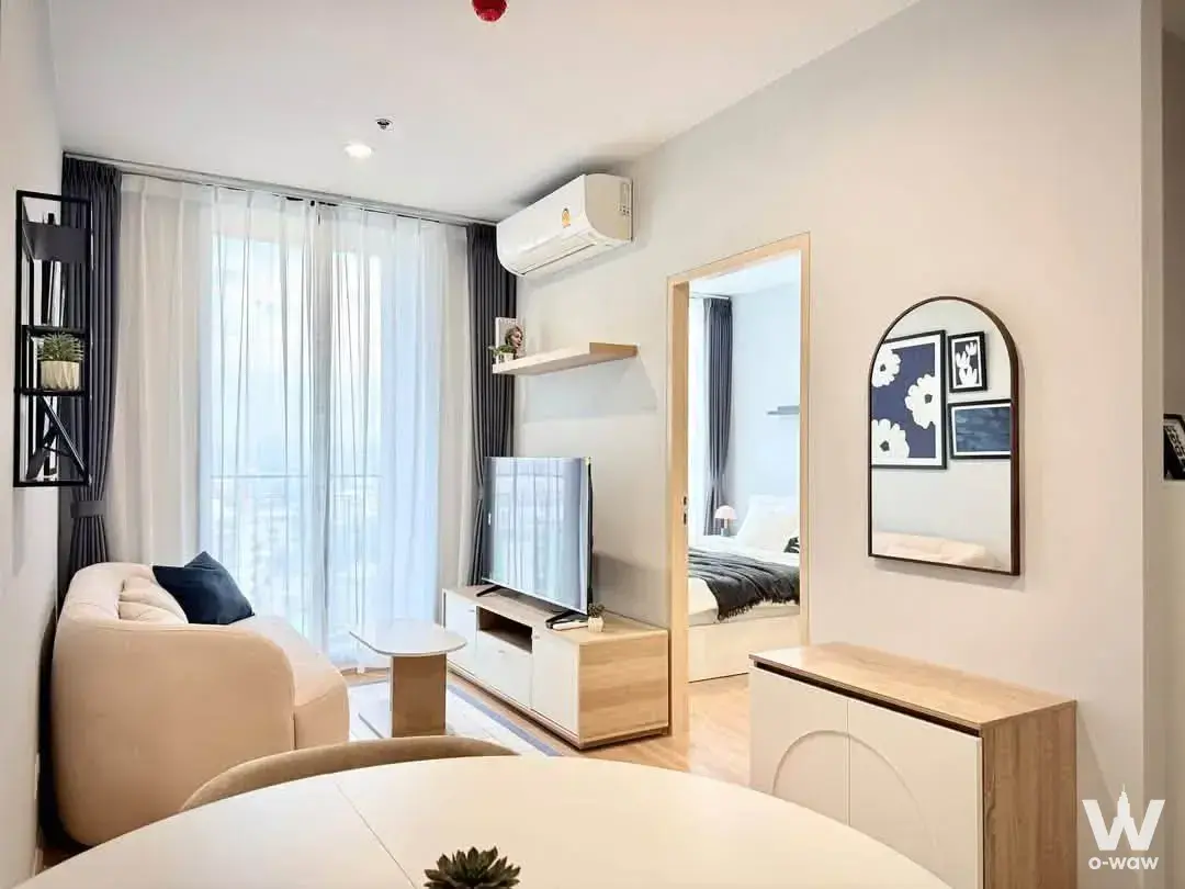 Living room with curved cream sofa and arched mirror in a fully furnished 1-bed condo for rent at Skyrise Avenue Sukhumvit 64