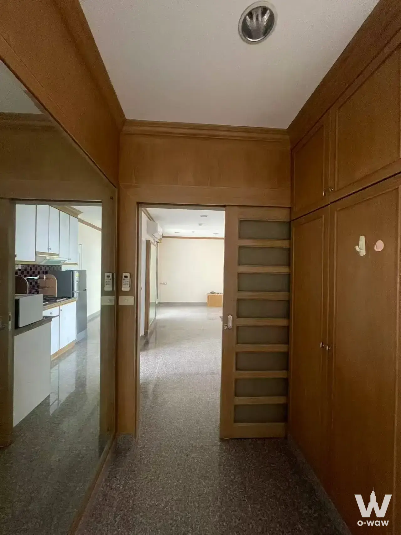 Pathum Wan Resort entry hallway with honey-toned wood paneling and terrazzo flooring