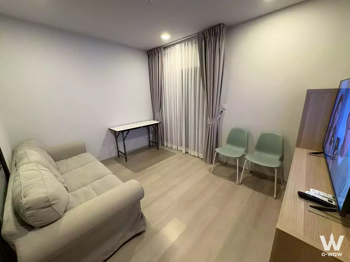 Compact living room in a Life Phahon-Ladprao rental with beige sofa, folding table, and floor-to-ceiling window