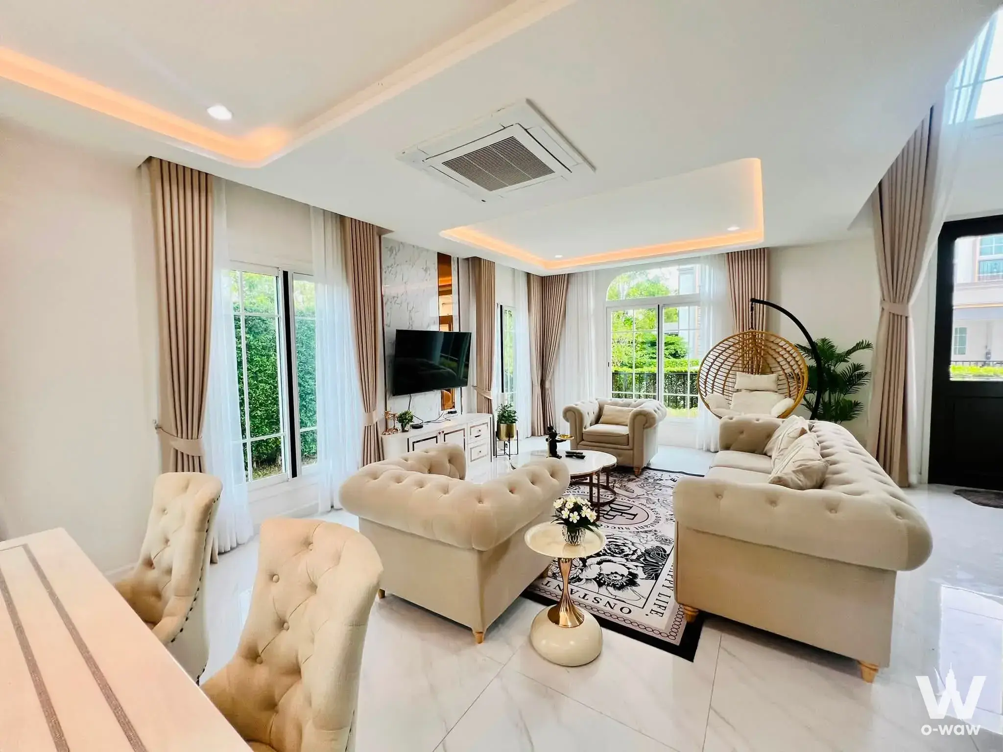 Bright living room in Grandio Bangna KM.5 house featuring cream Chesterfield sofa and rattan hanging chair