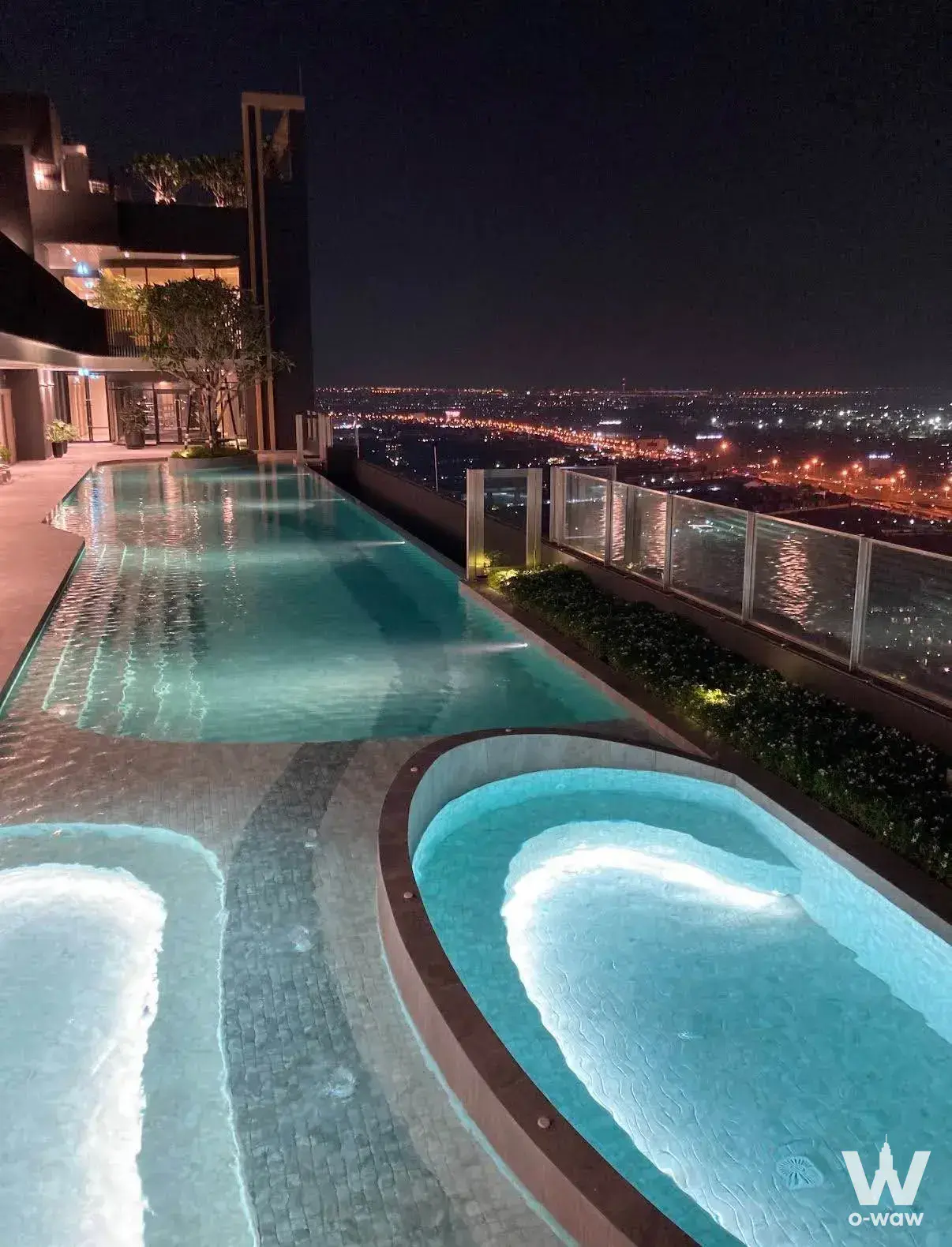 Rooftop infinity pool and jacuzzi at night with city views in this 1-bed condo for rent in Nue Mega Plus Bangna
