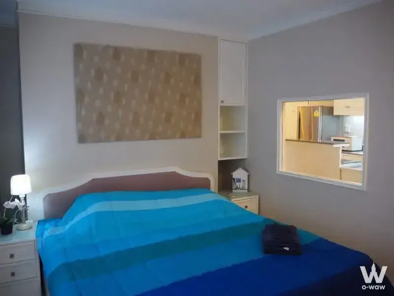 Bedroom with blue striped bedding and built-in shelving next to a pass-through window in a Saranjai Mansion condo