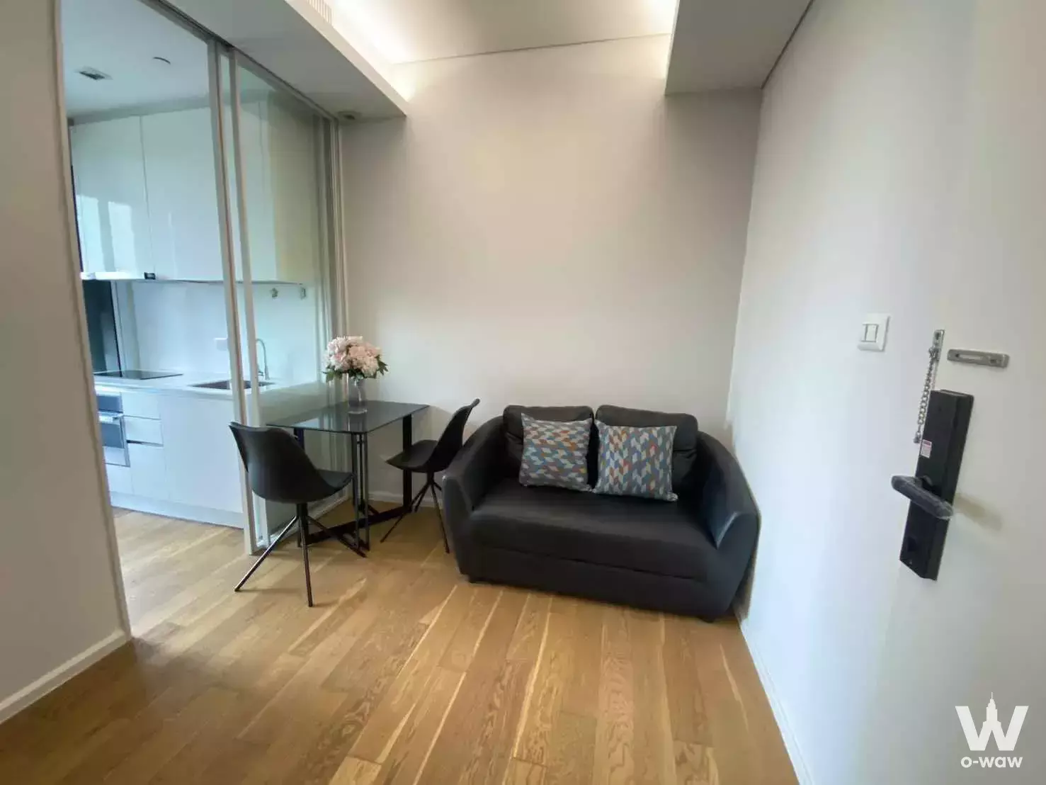 Furnished 1-bed condo in The Saint Residences featuring a grey leather sofa and glass partition separating the kitchen