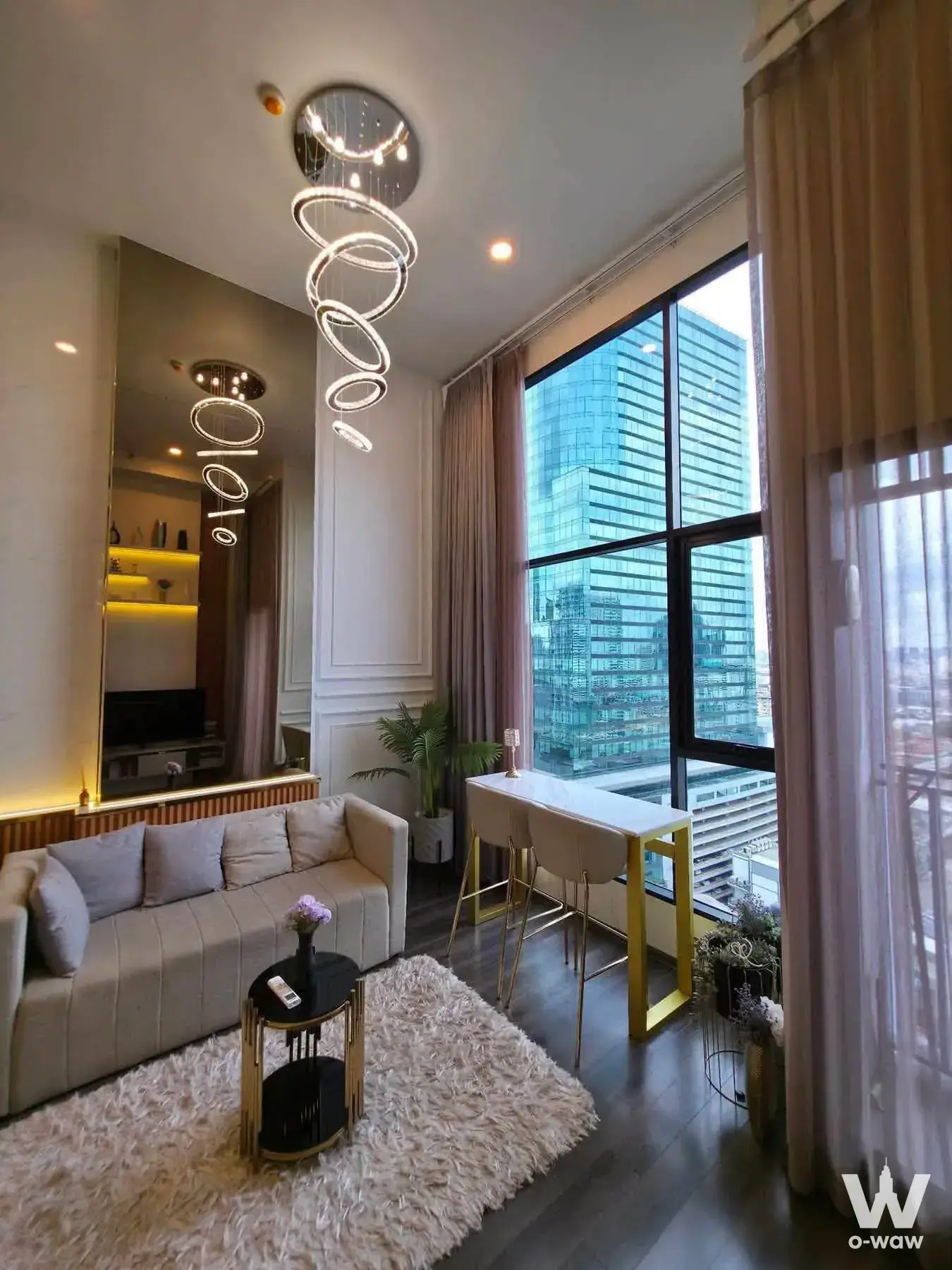 Living room in this Bangkok condo with floor-to-ceiling windows offering high-floor views of glass skyscrapers