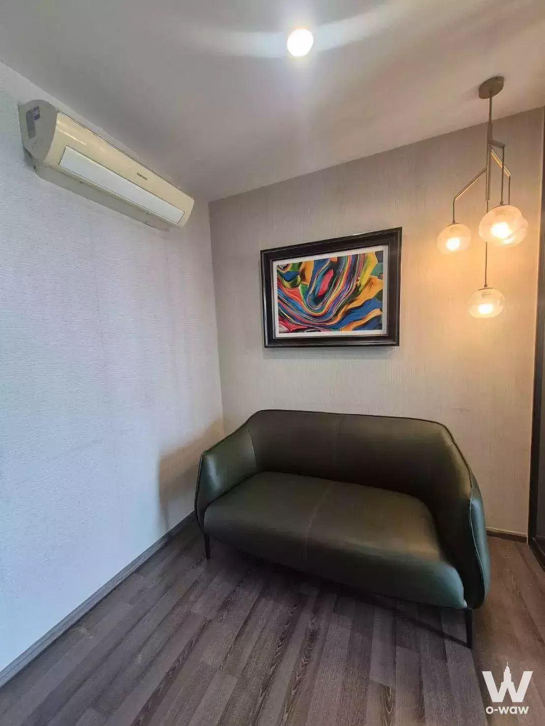 Compact sitting nook in THE BASE Park West condo with olive-green sofa, brass pendant lights, and abstract art