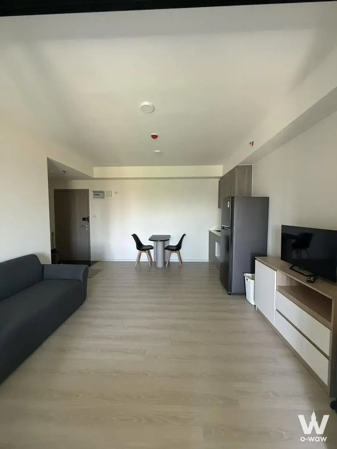Open-plan living area in a 1-bed rental at A Space Mega 2 with grey sofa, dining nook, and compact kitchenette