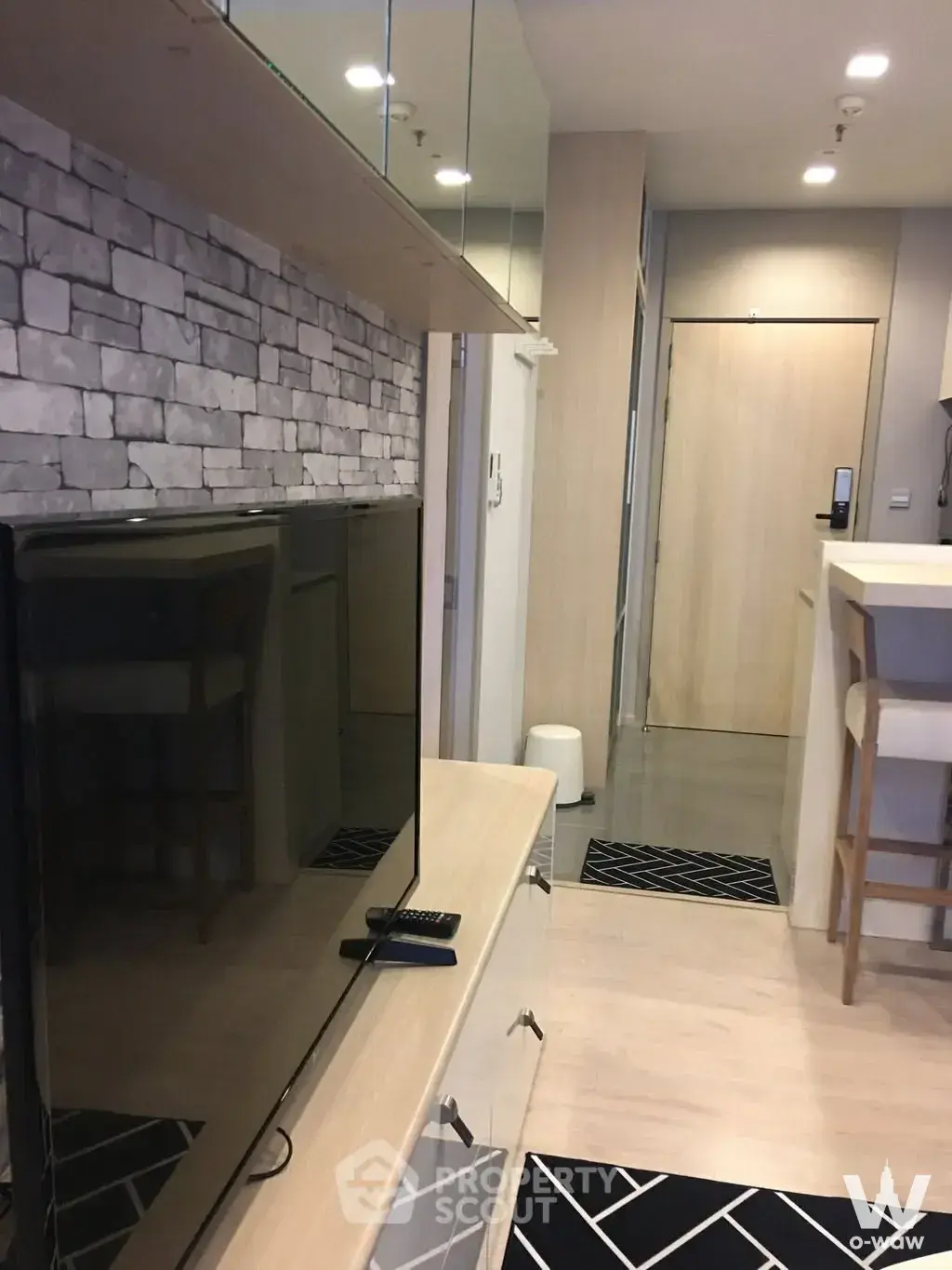 Modern 1-bed condo for rent in M Thonglor 10 featuring a faux stone accent wall and light wood flooring