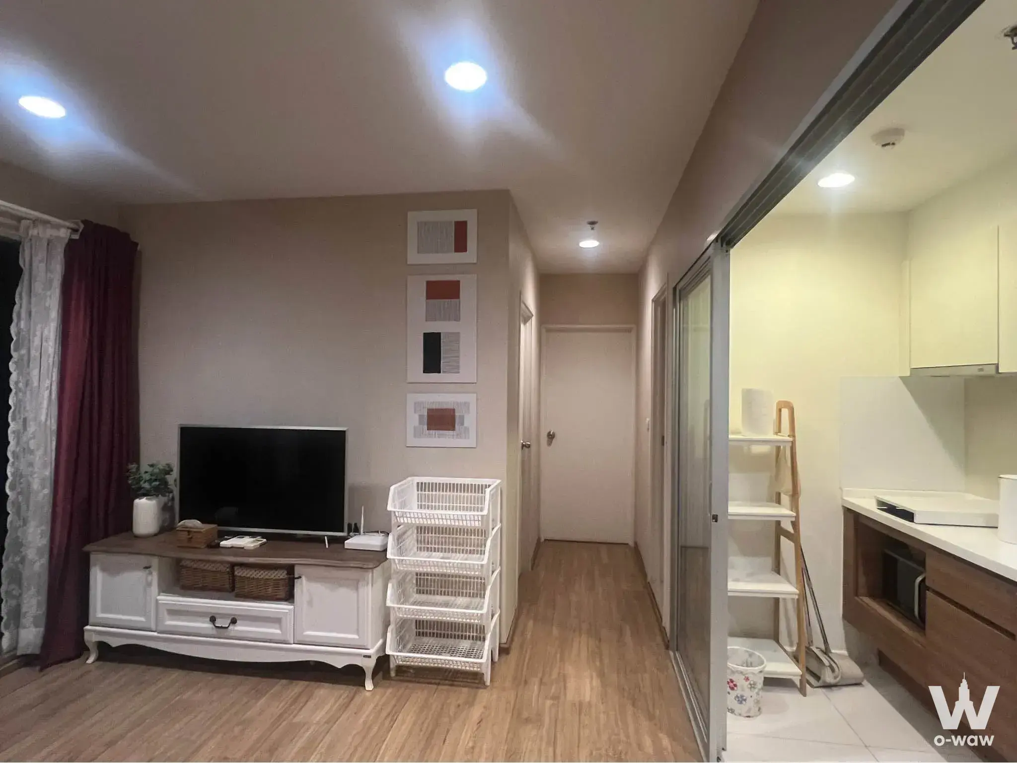 Living room with TV console and maroon curtains overlooking open kitchen in Fuse Chan Sathorn