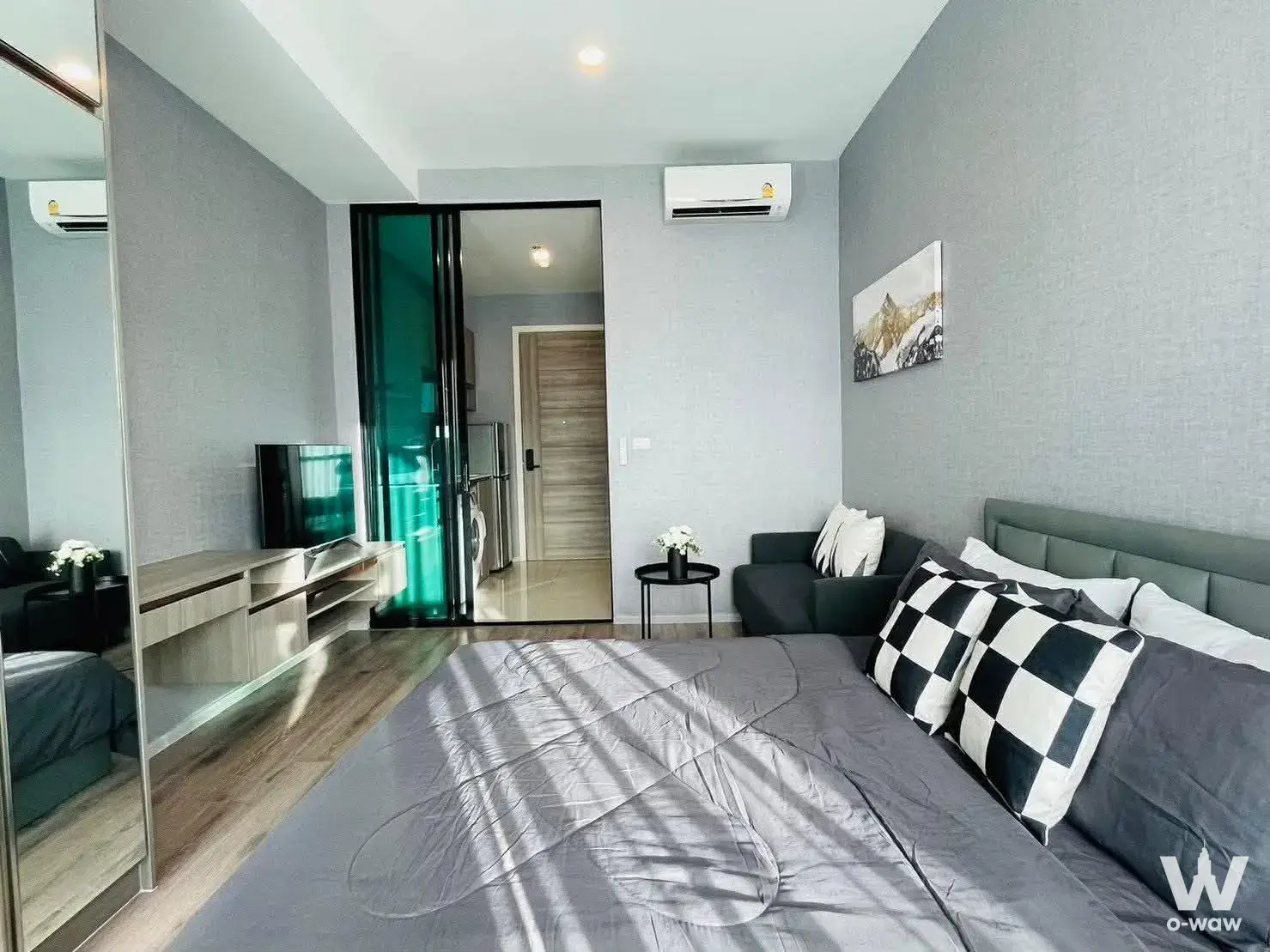 Compact studio bedroom featuring grey sofa, checkered pillows, and teal glass partition in KnightsBridge Collage