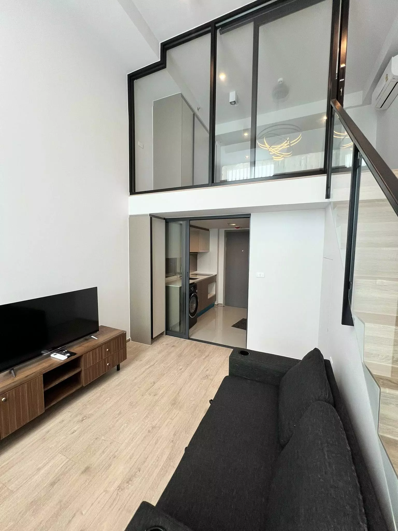 Double-height living room in IDEO Rama 9 condo with mezzanine, glass partition, and modern loft style