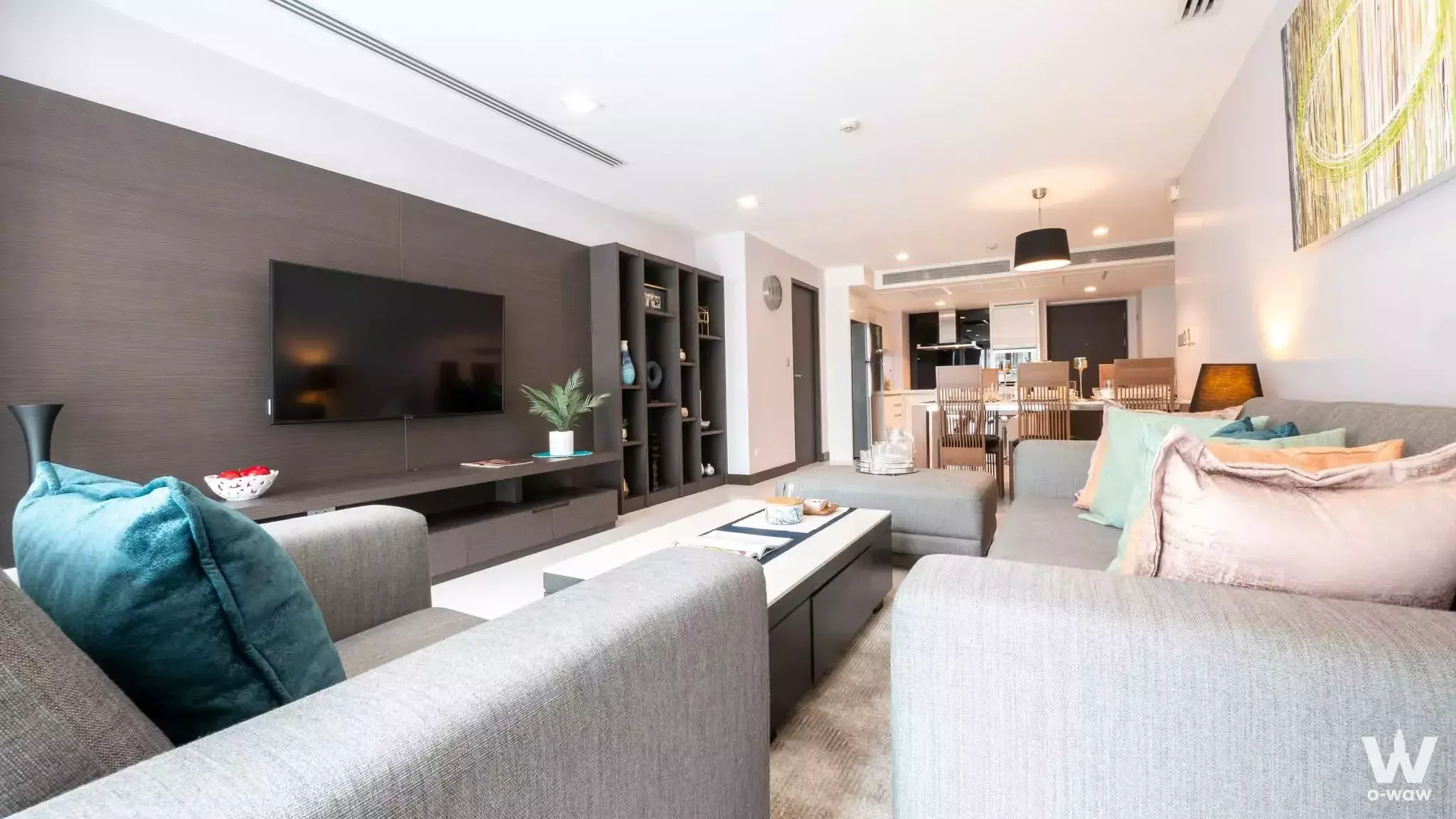 Open-plan living room in The Klasse Residence condo featuring a grey L-shaped sofa and teal accents