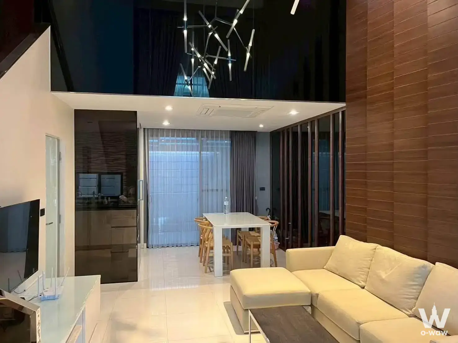 Open-plan living room in Baan Klang Mueang townhouse with cream sectional sofa, high ceiling, and pendant light