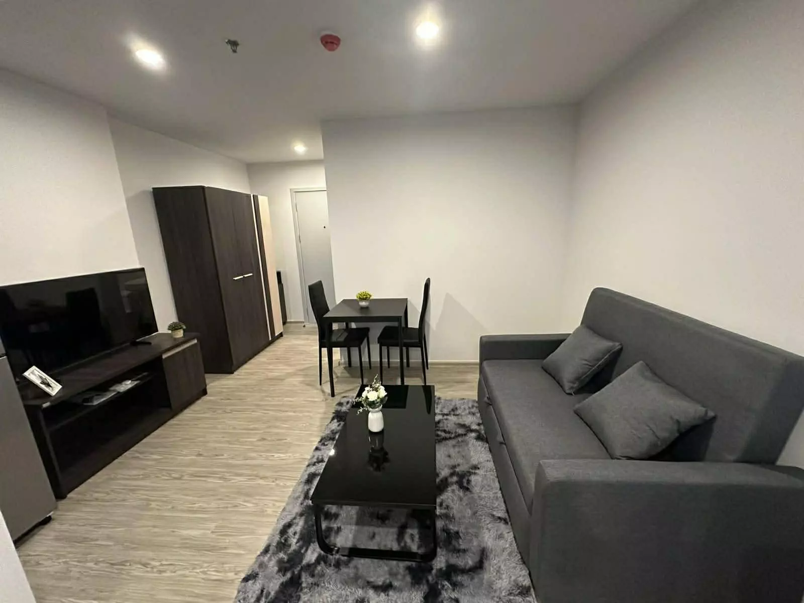 Furnished Regent Home Bangna unit with dark grey sofa, black coffee table, and dining set in neutral tones
