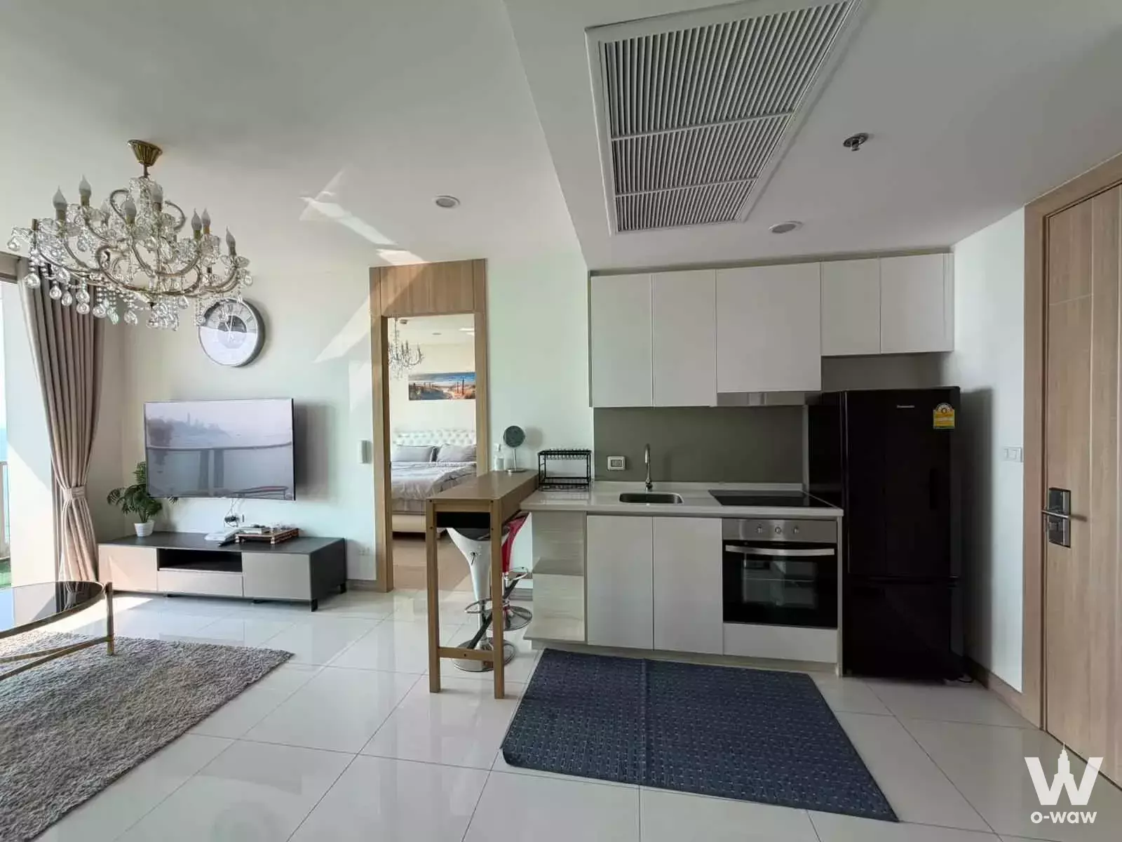 Open-plan living room and kitchenette with crystal chandelier in a 2-bed condo for rent at The Riviera Wongamat Beach