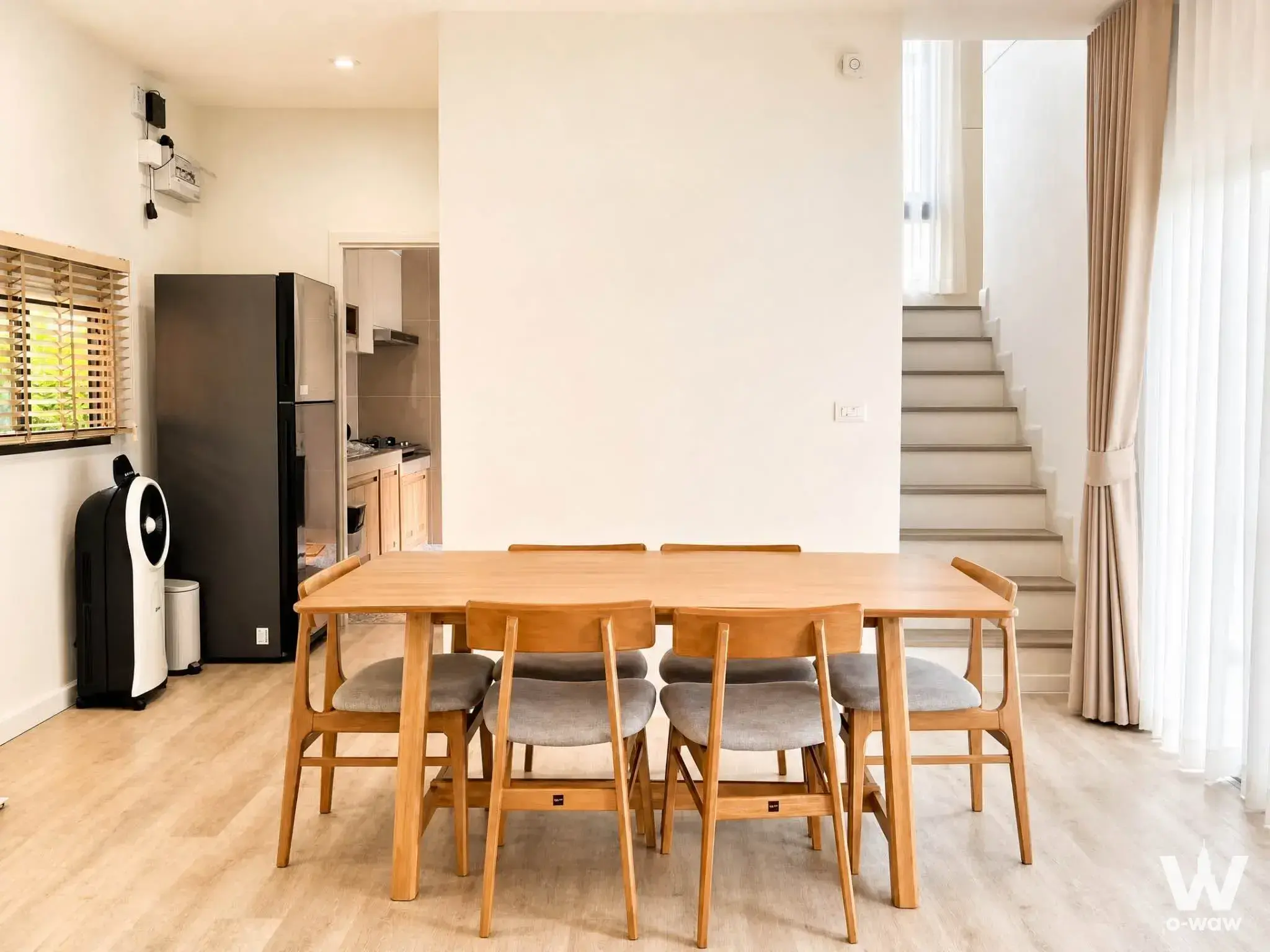 Dining area in a Saransiri Westgate condo featuring light oak table and open-plan kitchen view