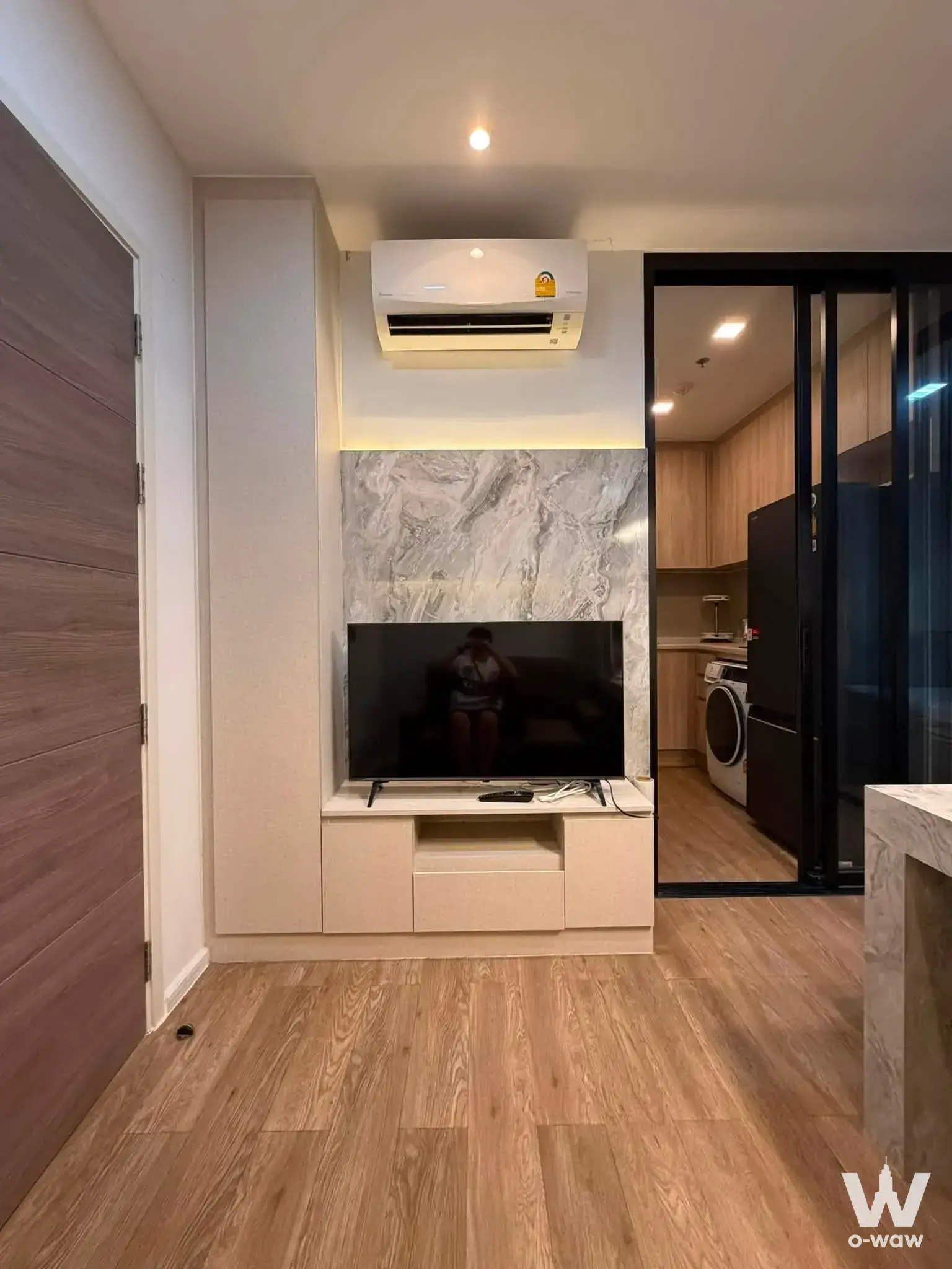 Modern living room in Modiz Sukhumvit 50 featuring marble TV panel and open kitchen view