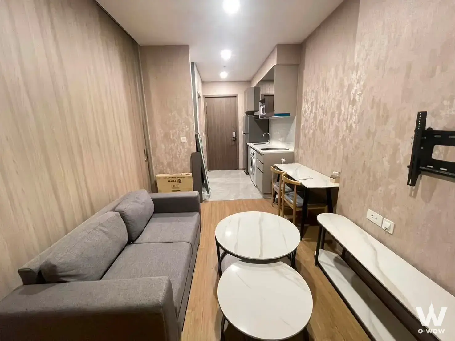 Cloud Thonglor-Phetchaburi 1-bed condo living area with grey sofa, nested marble coffee tables, and minimalist kitchenette