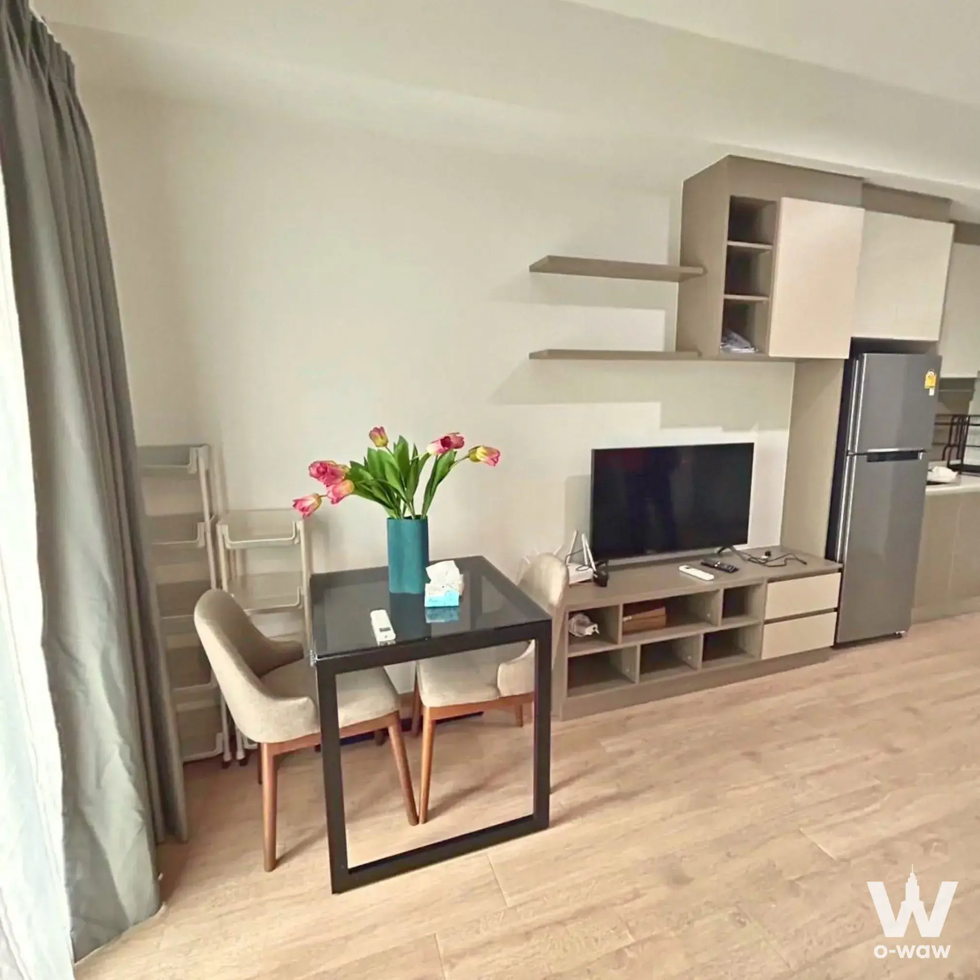 Modern 1-bed condo living area in IDEO Rama 9 featuring a black glass dining table, beige chairs, and built-in cream