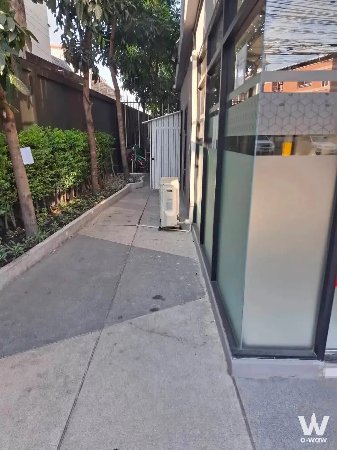 Narrow concrete side alley with glass facade and hedge outside this 0-bed condo for sale at IKON Sukhumvit 77