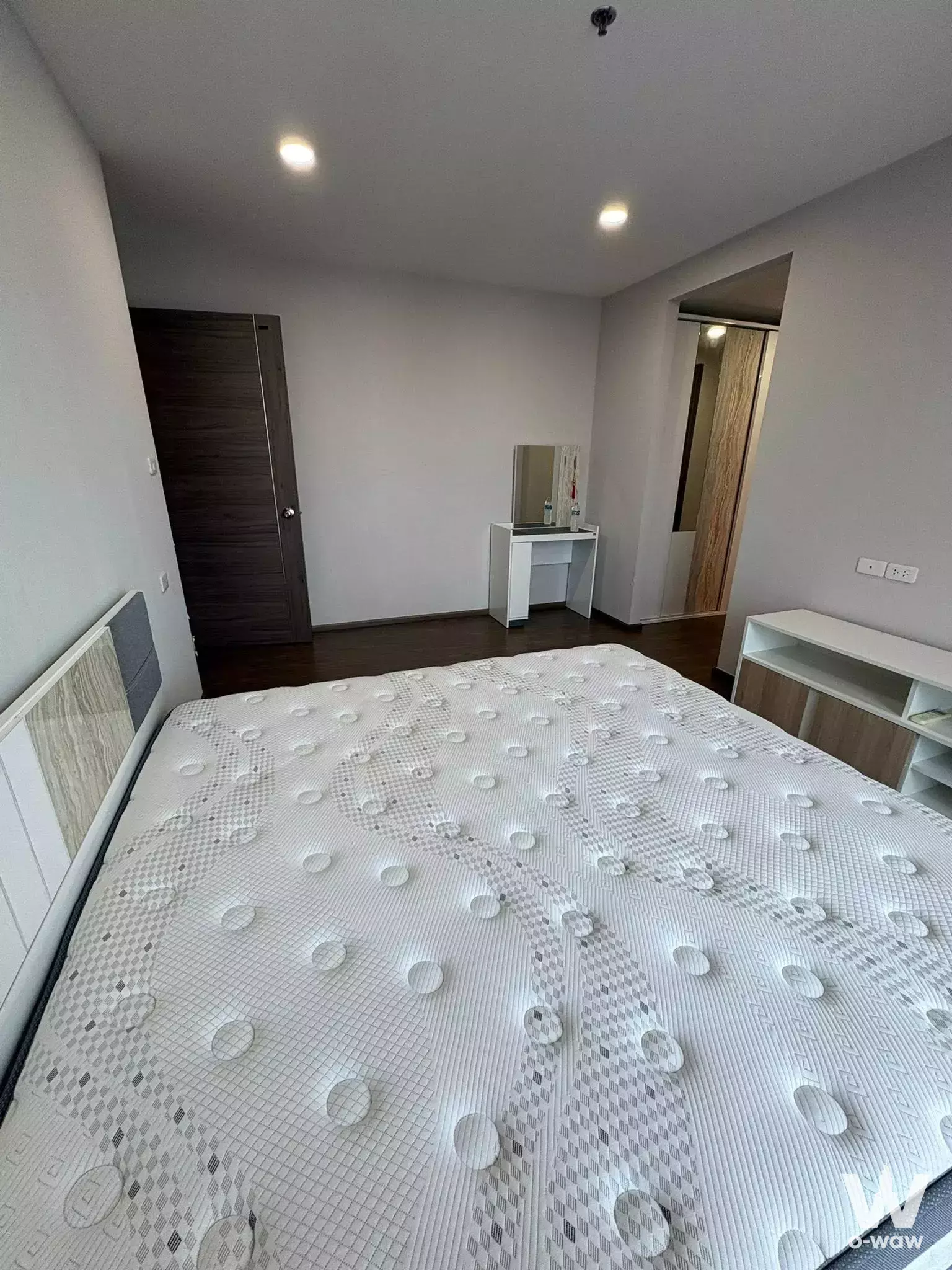 Bedroom in an Artisan Ratchada unit with a white tufted bed frame, dark walnut door, and light grey walls
