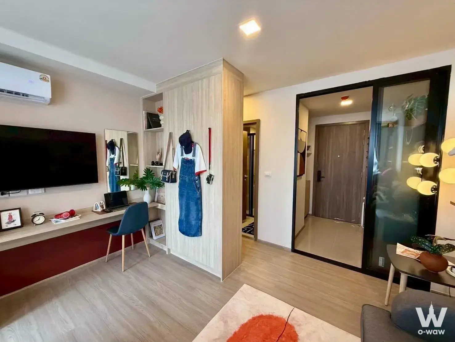 Studio living space in THE MUVE Sukhumvit 107 with wall-mounted TV, floating desk, and tall light-wood storage divider