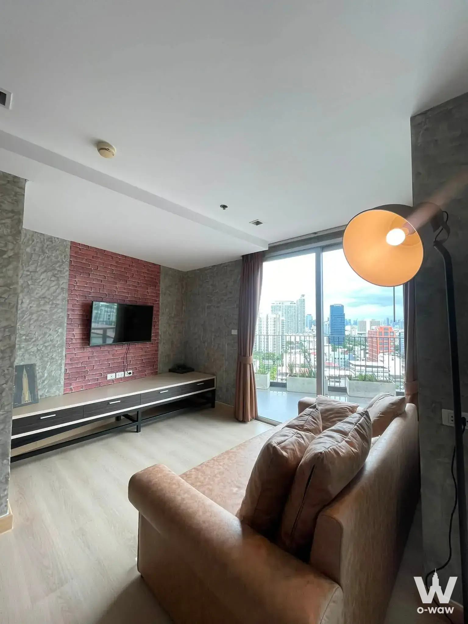 Living room in a 1-bed condo at Haus 23 Condo with tan leather sofa, red brick accent wall, and high-rise skyline views