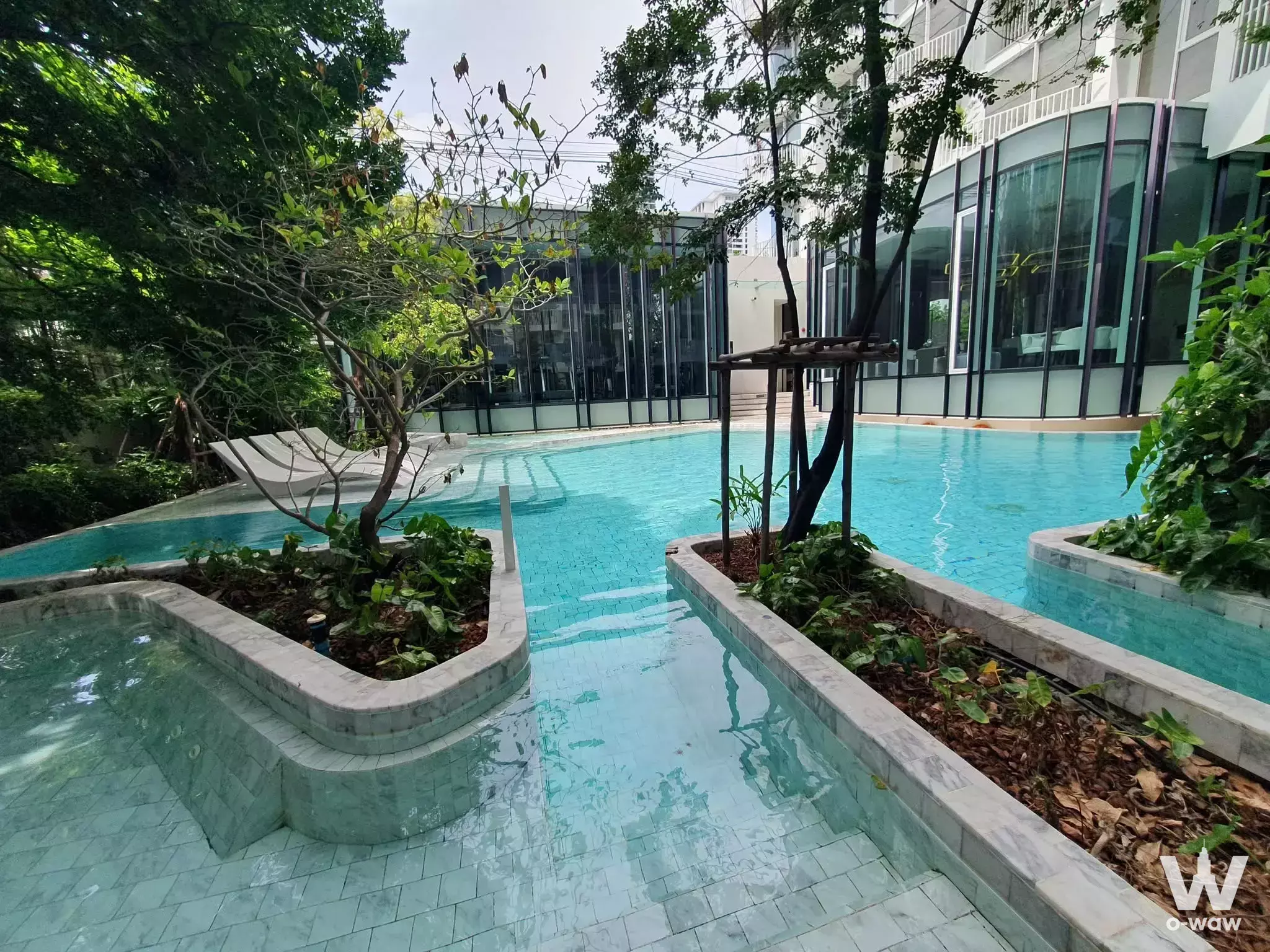 Resort-style outdoor pool with turquoise water and a central planter island at Chewathai Residence Thong Lo