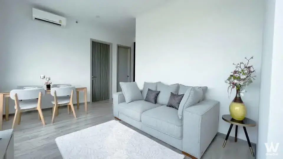 Open-plan living area in KnightsBridge Prime Onnut with a light-grey sofa, wood-look flooring, and a four-seat dining set