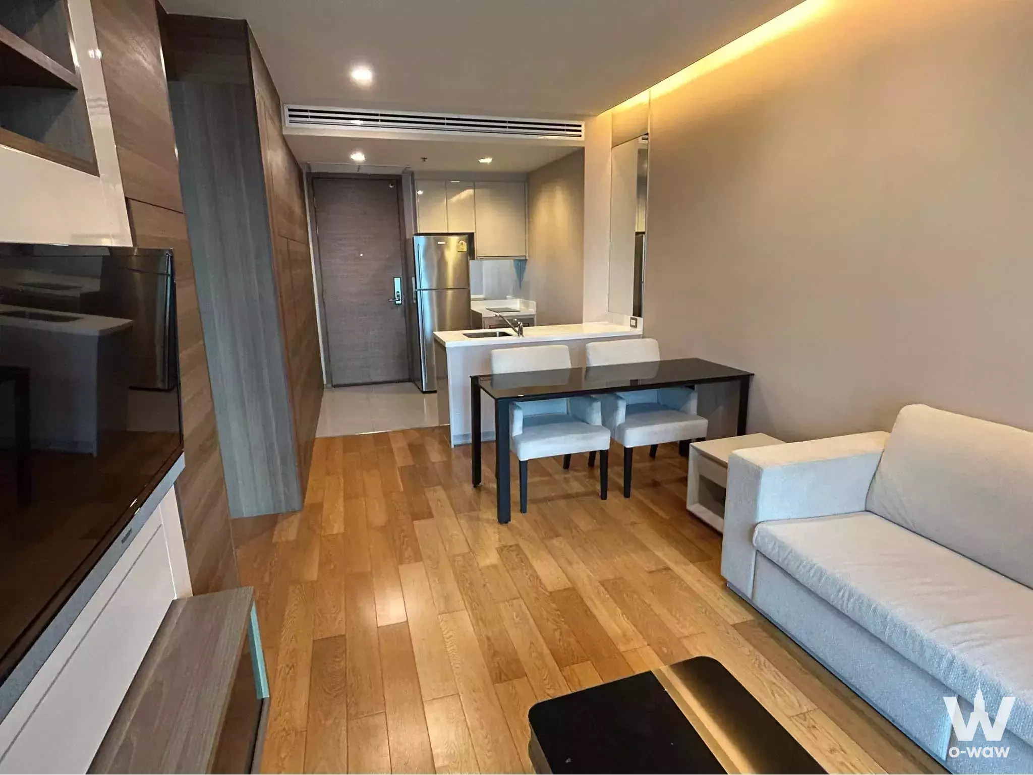 Open-plan living area with grey sofa and glass dining table in The Address Sathon 1-bed condo for rent