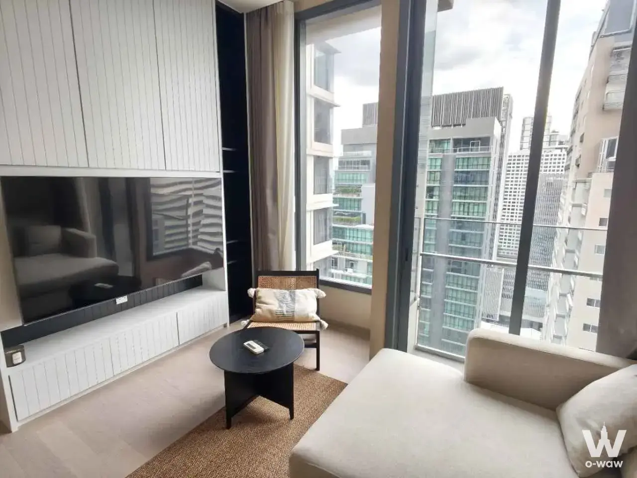 1-bed condo for rent in THE ESSE ASOKE living room with built-in white cabinetry, TV, rattan armchair, sofa, and high-rise