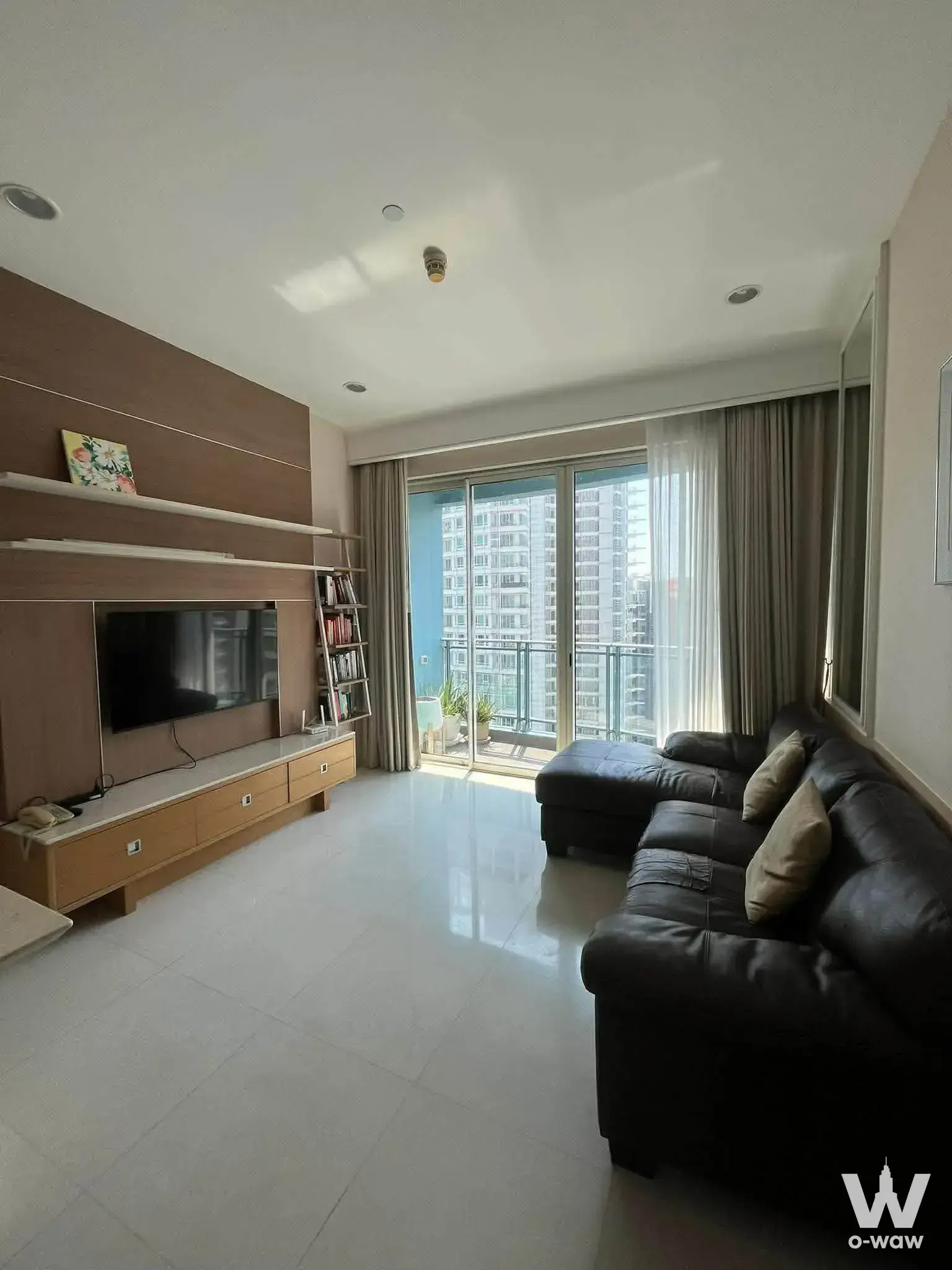 Living room in Q Lang Suan condo with black sectional sofa and balcony access