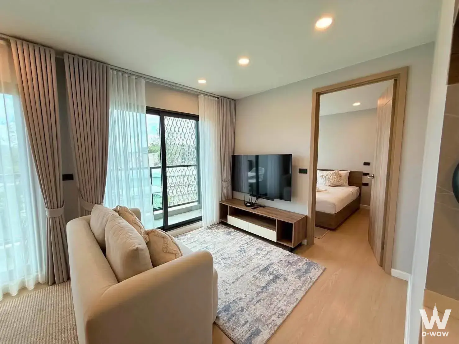 Living room in a Space Cherngtalay 2-bed condo showing beige sofa, media console, and bedroom access