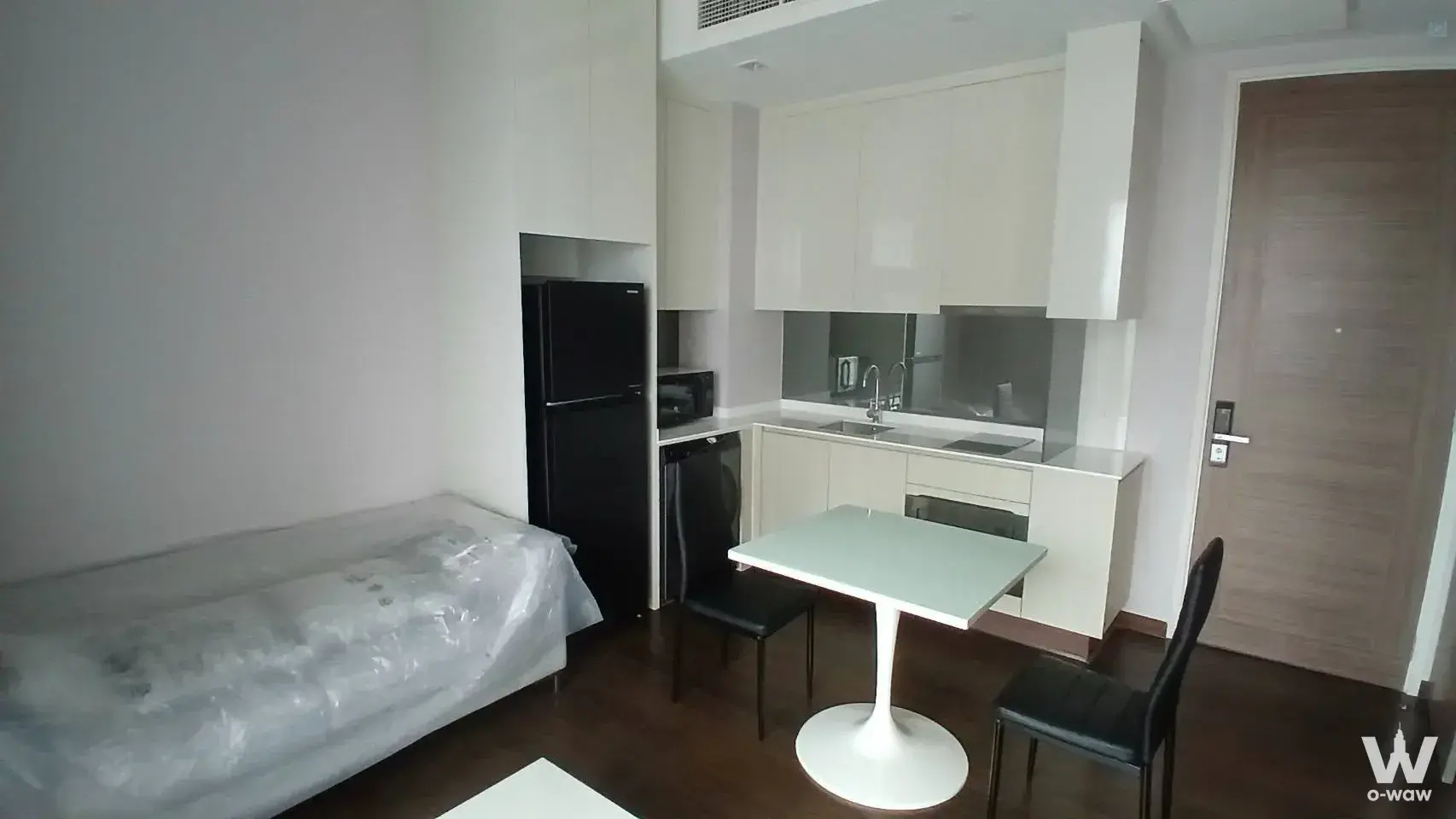 Open-plan kitchenette with cream cabinets and black appliances in a Q Asoke studio
