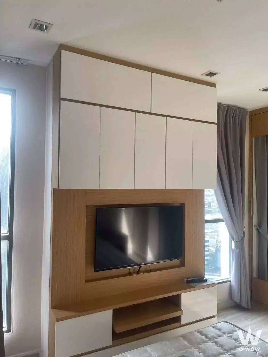 Bright bedroom in Ideo Mobi Rama 9 with floor-to-ceiling oak cabinetry, recessed TV, and city views