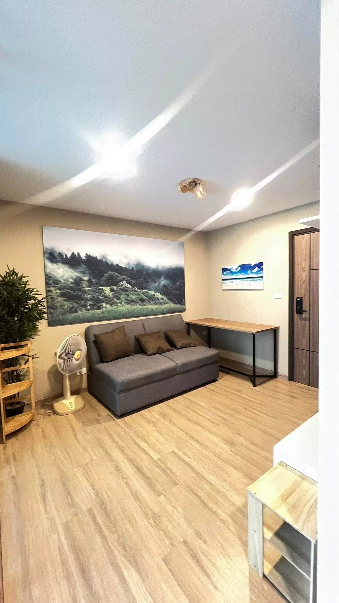 Living room in a The Cube South Chaeng Watthana 1-bed condo with grey sofa, oak floors, and landscape art