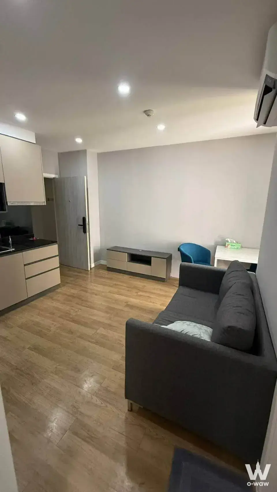 2-bed condo for rent in Groove Ratchada-Rama 9 open-plan unit with light wood flooring, grey sofa, and beige kitchen cabinets