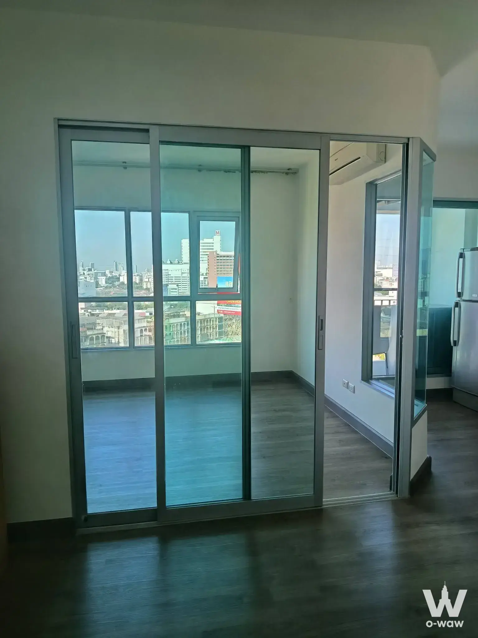 The empty living room has dark wood floors and a glass balcony in a 1-bed condo for sale at Aspire Ngamwongwan