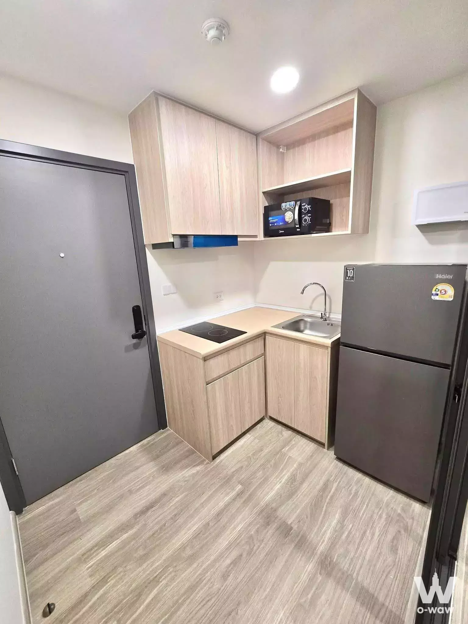 Unfurnished kitchenette in a 1-bed condo for rent at Beat Sukhumvit with L-shaped light-oak cabinetry and neutral minimalist