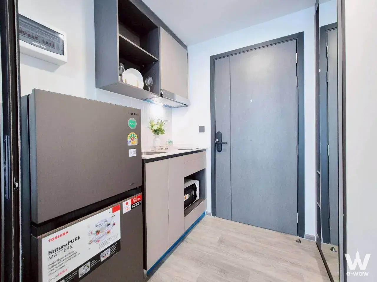 Compact kitchenette in an Atmoz Palacio Ladprao condo featuring dark fridge, black countertop, and built-in microwave
