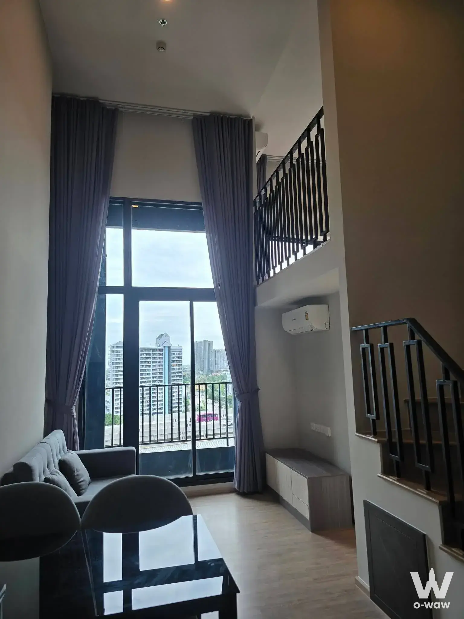 The duplex living area in a 1-bed condo for sale at Ken Attitude Rattanathibet has a grey sofa, dining table and skyline view