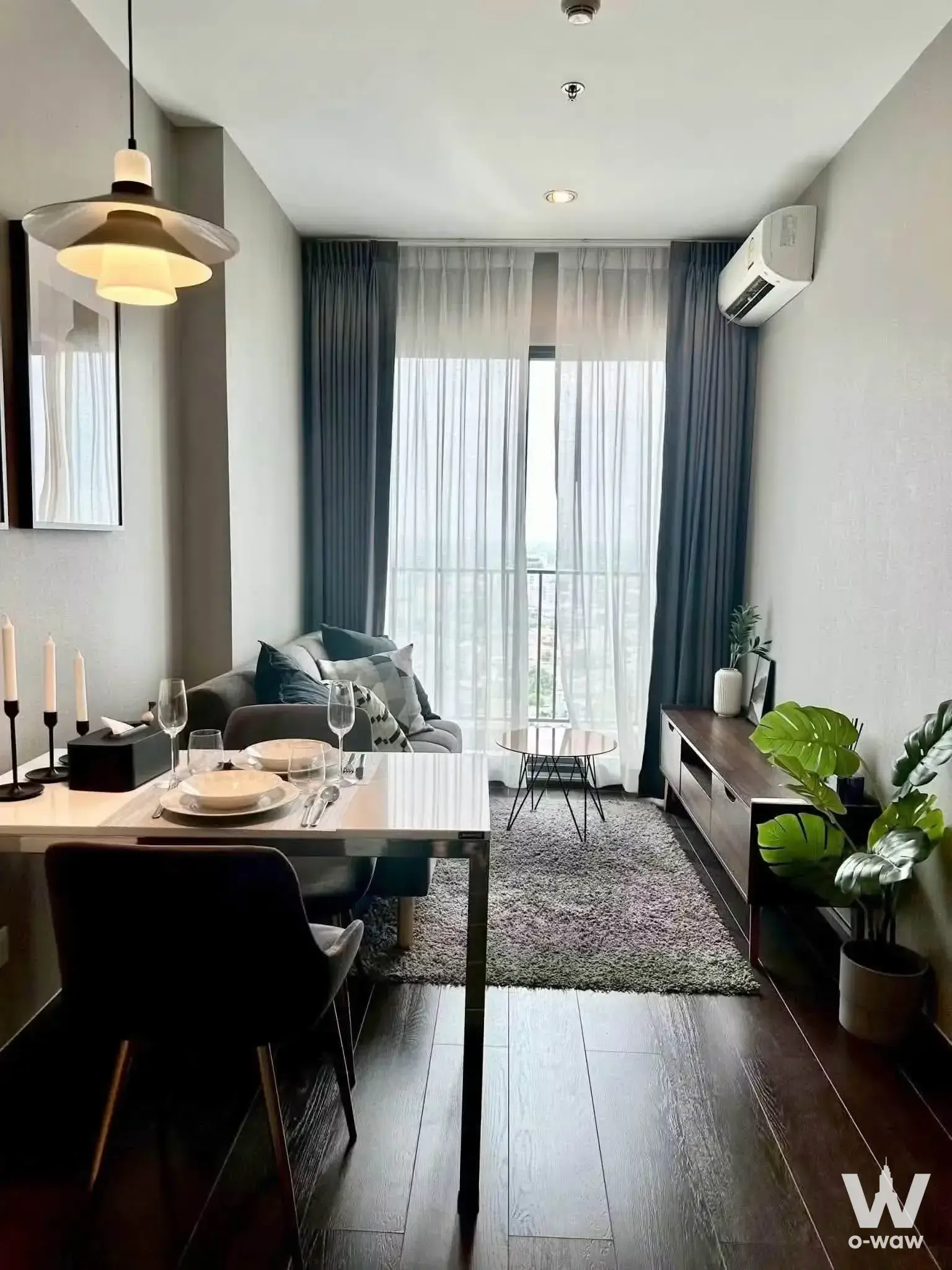 Dining-living combo in C Ekkamai Condominium with dark wood floors, grey sofa, and floor-to-ceiling windows
