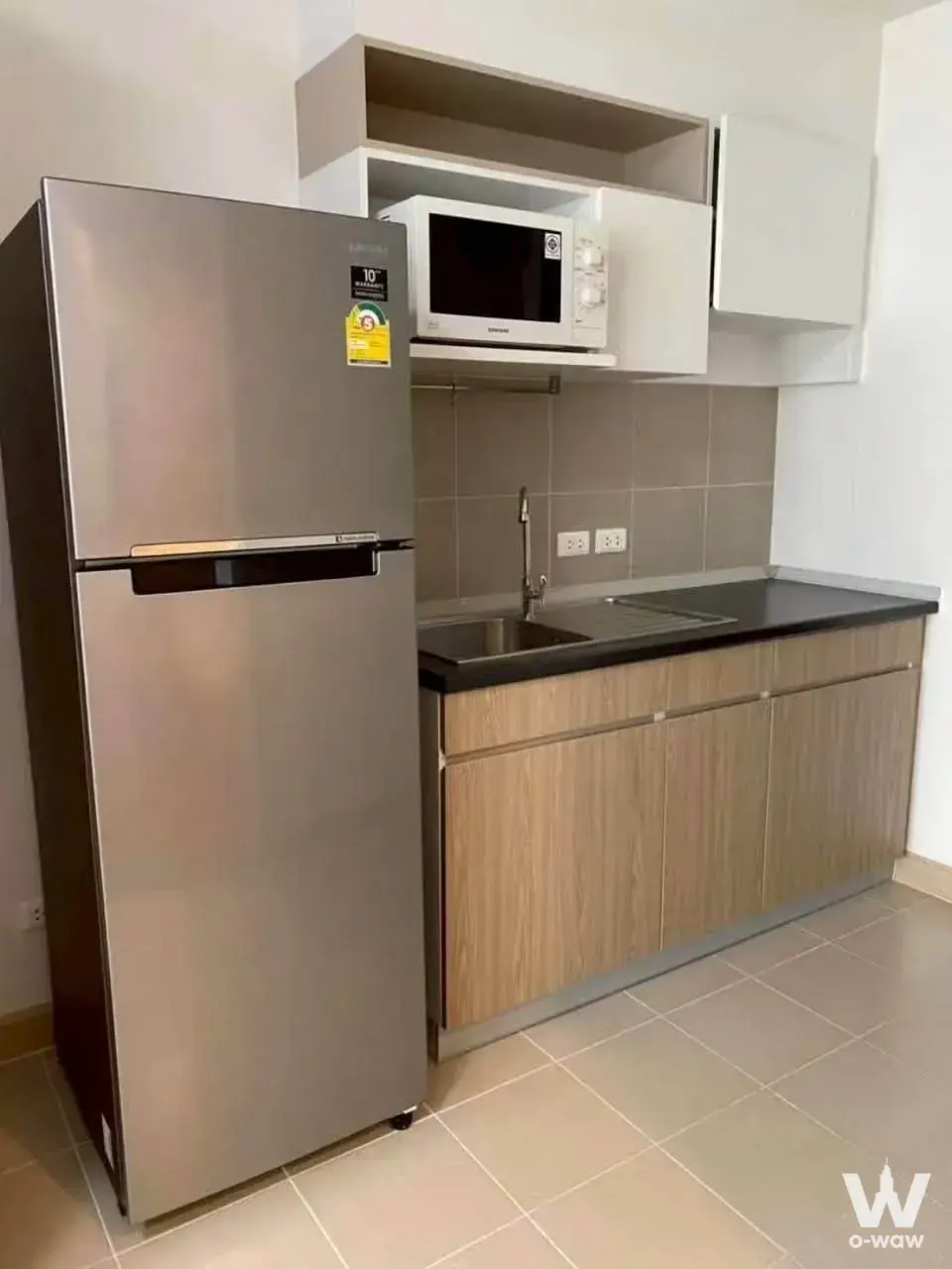 Compact kitchen with oak cabinets, black countertop, and stainless fridge in a 1-bed condo for rent at Supalai Veranda Rama 9