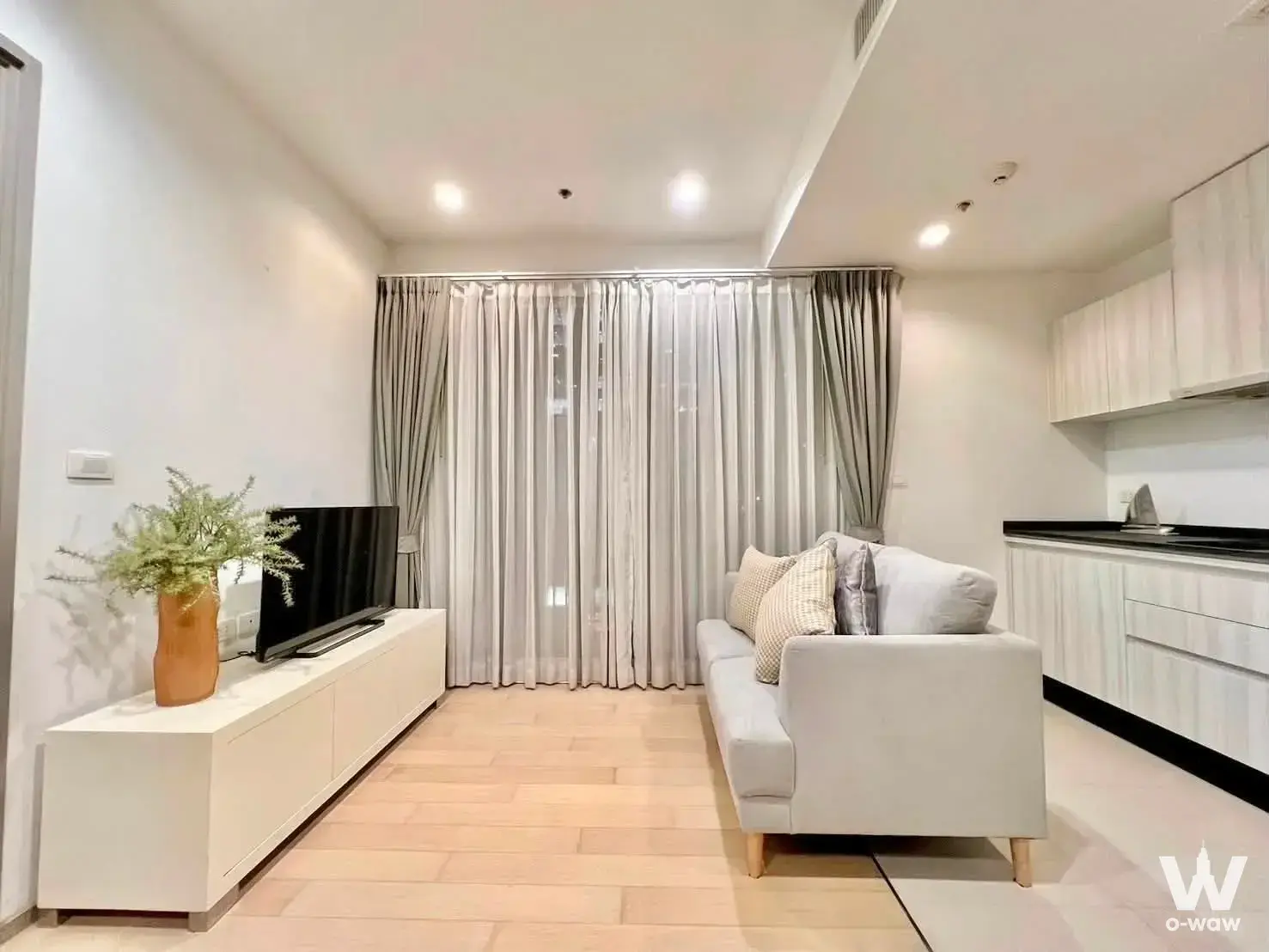 Living area in HQ by Sansiri condo featuring grey sofa, terracotta vase, and open kitchen access