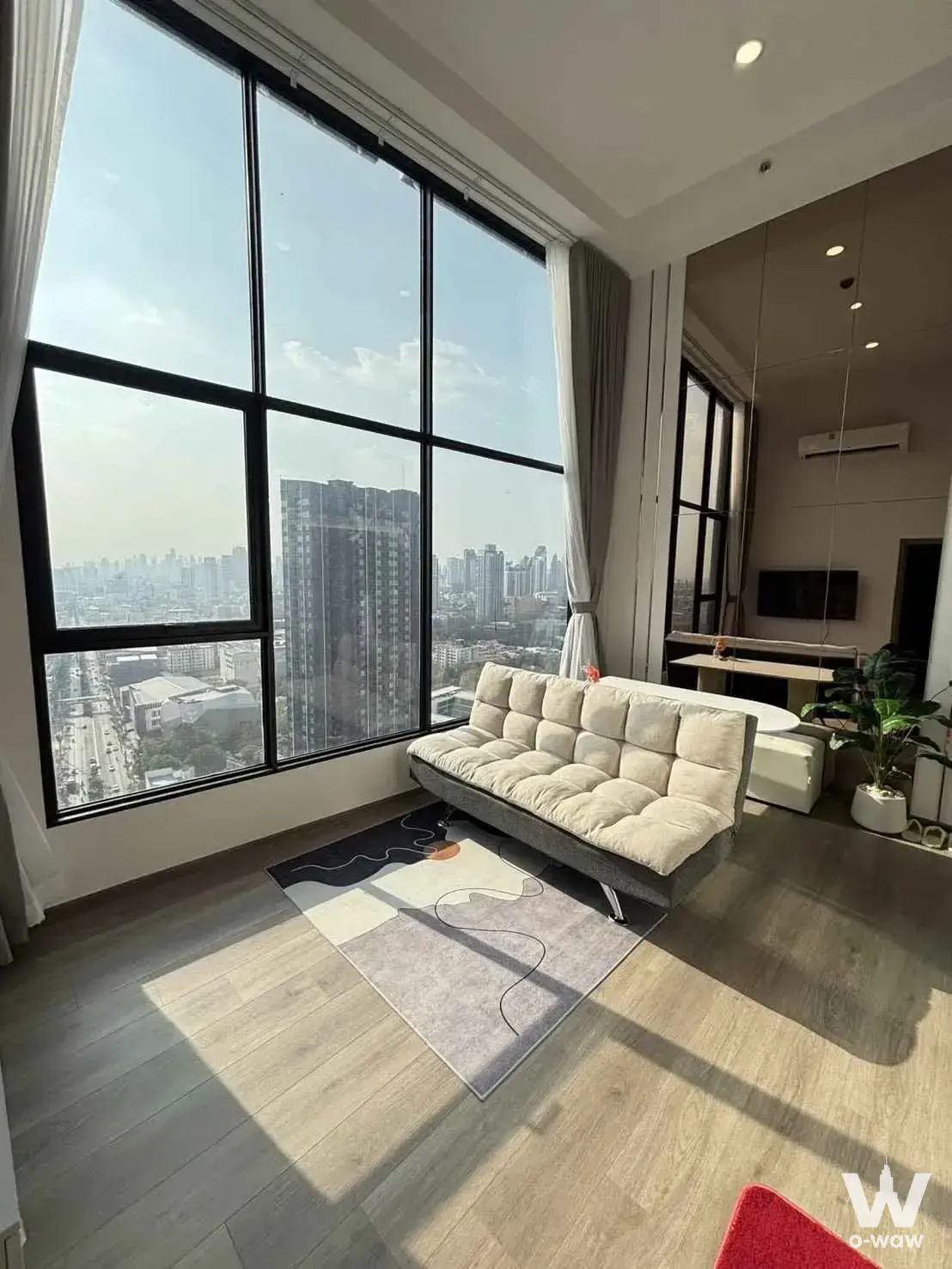 Living room with tufted sofa and city views in a 2-bed condo for rent at KnightsBridge Space Sukhumvit-Rama 4