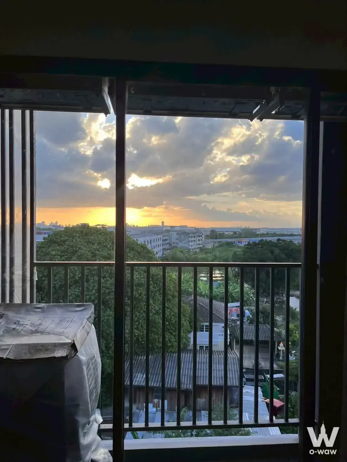 High-floor balcony view showing a sunset sky, dense green canopy, and distant city skyline from SO Origin Phahol 69 Station